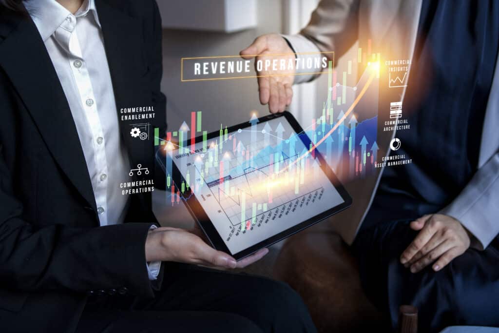 Two business professionals analyzing a digital graph on a tablet showing revenue operations and growth trends, with holographic data projections.