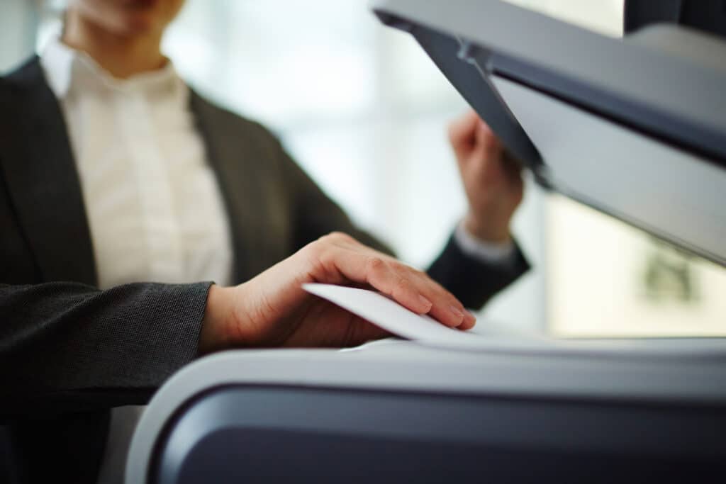 A person in business attire inserting paper into a printer or copier, focusing on their hands and the paper tray.